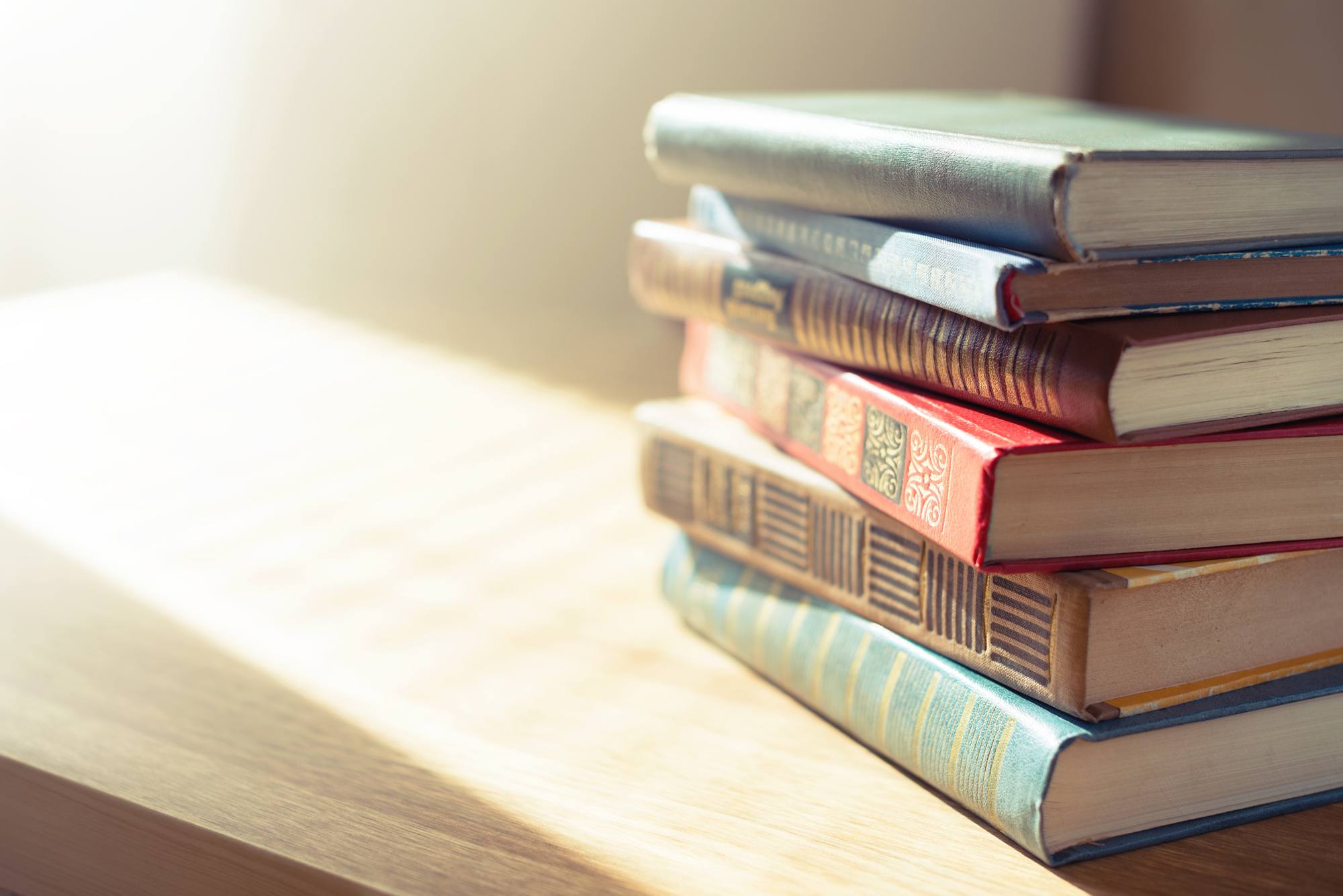 Stack of vintage hardcover books on a sunlit wooden surface with space for text on the left.