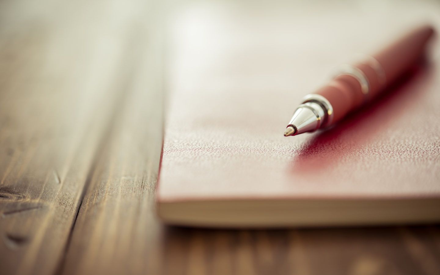 Red pen resting on a closed notebook on a wooden table.