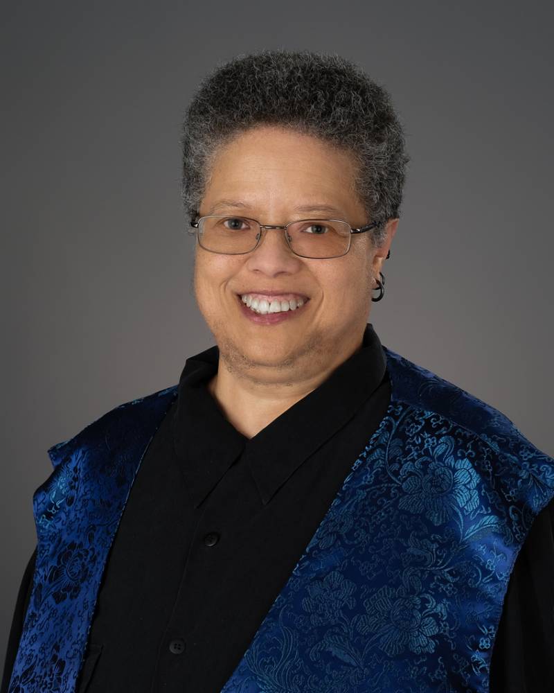 Professional headshot of a smiling woman wearing glasses against a light background.